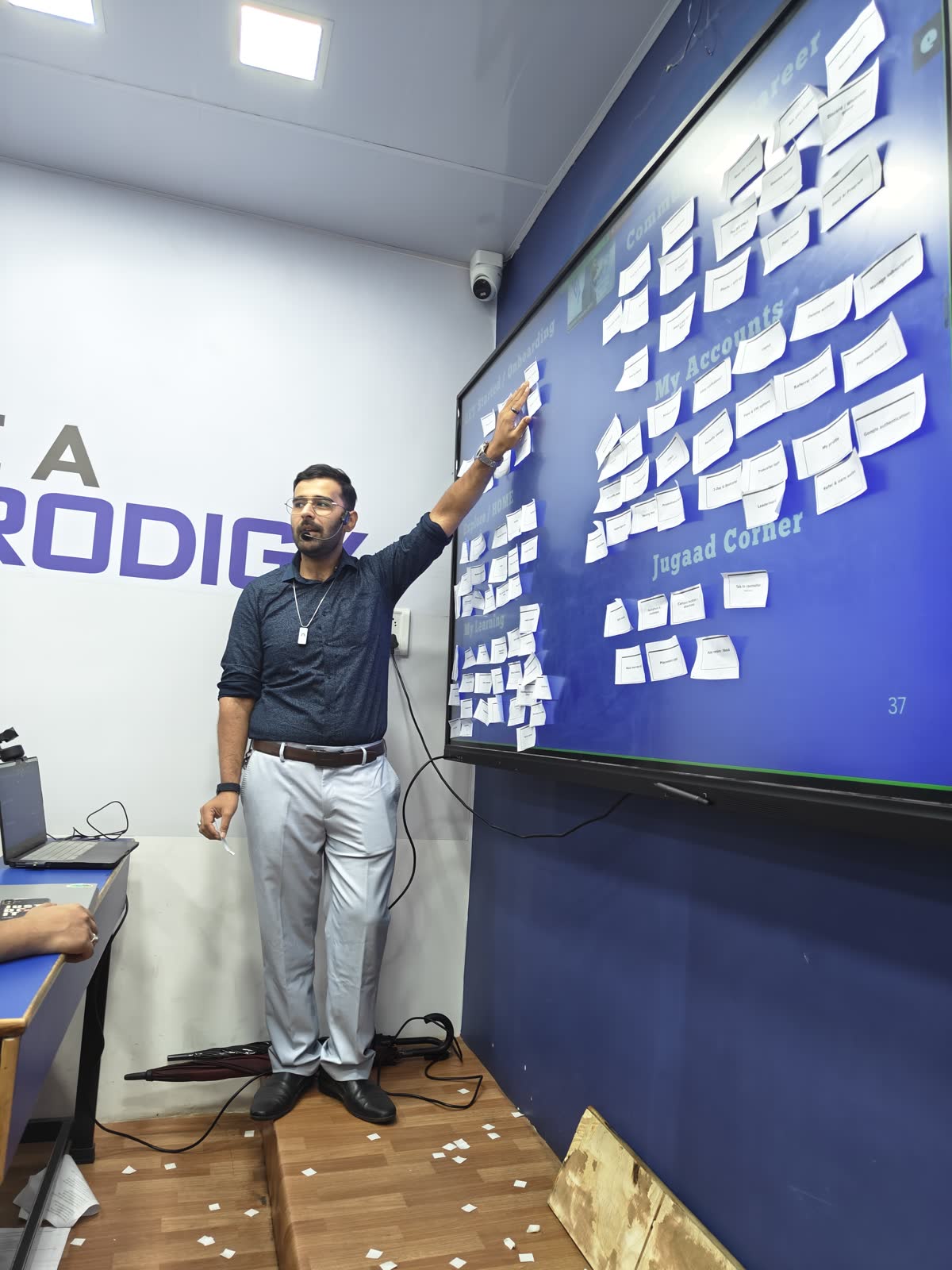 Ali pointing at a wall of sticky-note ideas in the DIT classroom